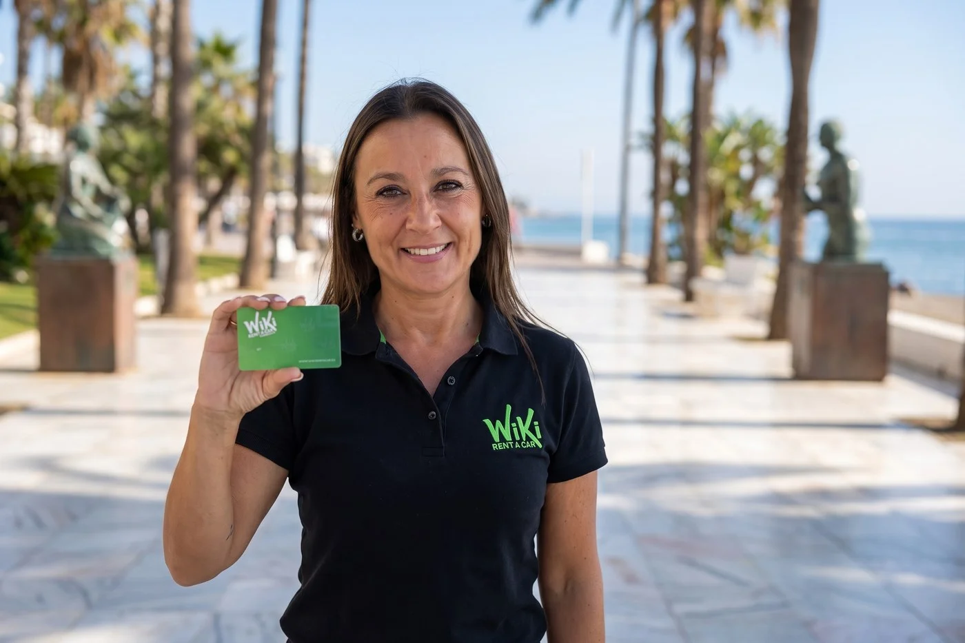Wiki Rent A Car staff member holding the customer card on the Marbella seafront promenade, car hire pick-up point